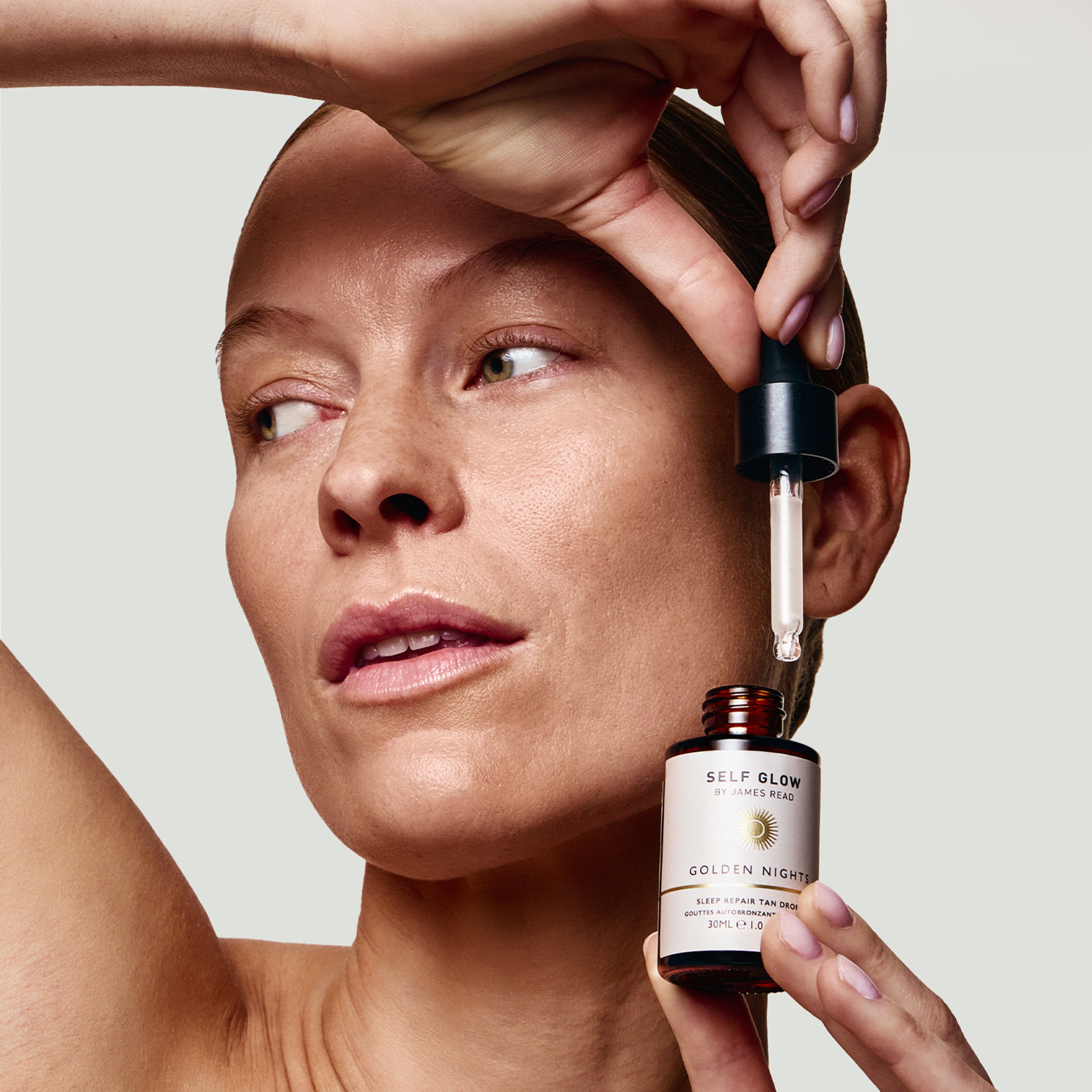 Woman applying a skincare serum to her face with a dropper bottle labeled 'Self Glow'.