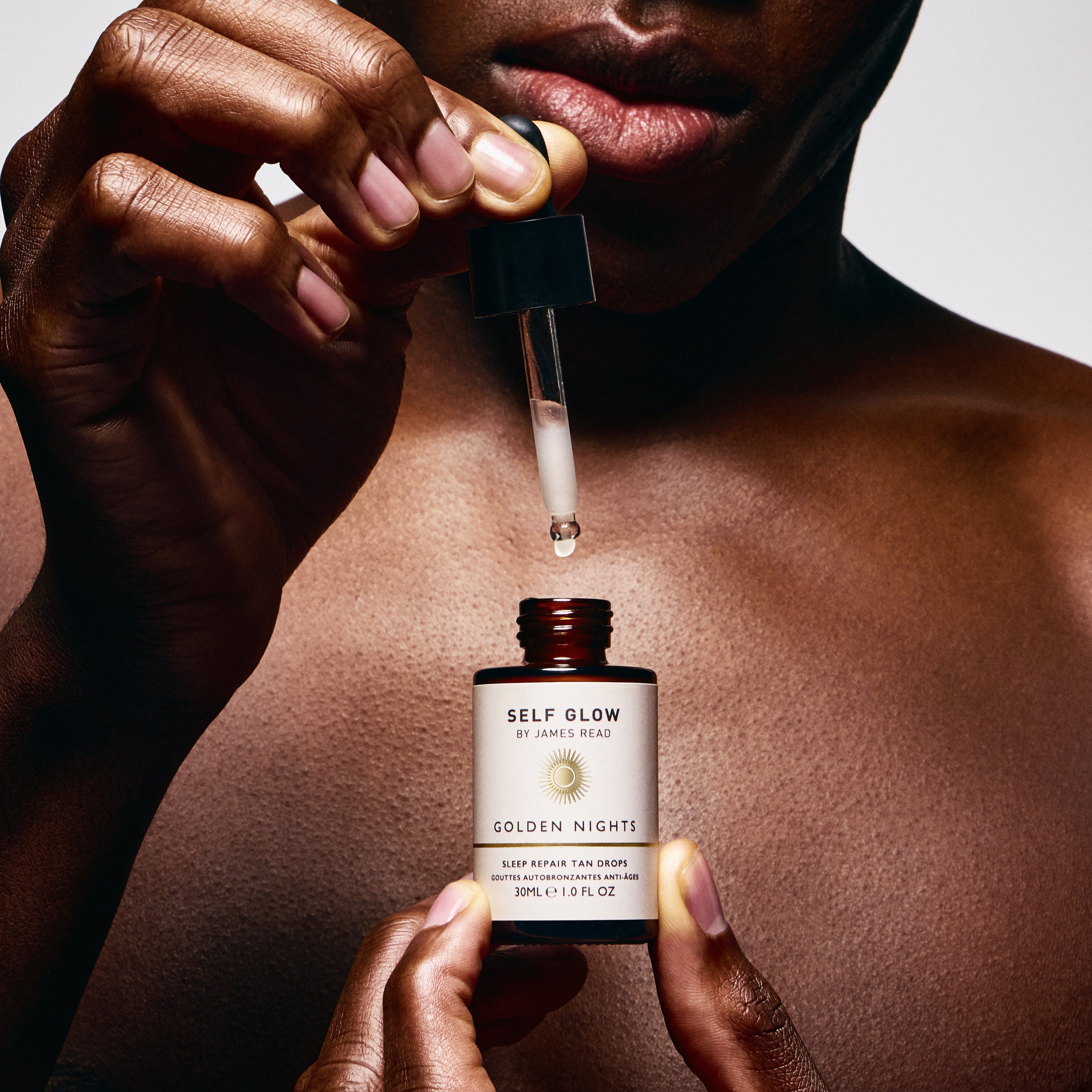 Person holding a dropper over a bottle labeled 'Self Glow' with a neutral background